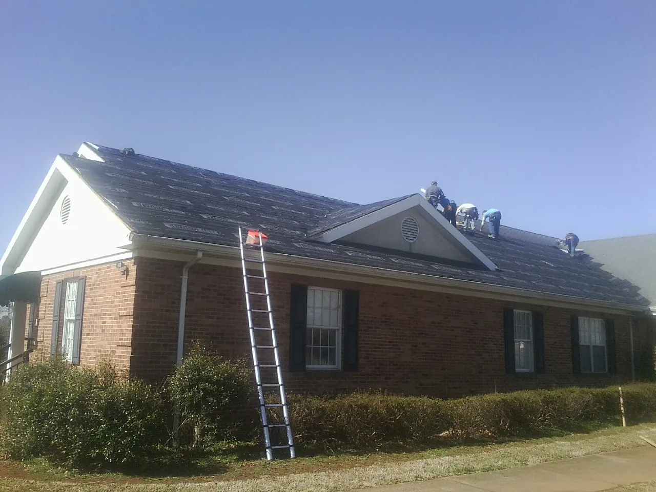 Crew tearing shingles off a brick ranch roof with a ladder set — Emergency Roof Repair work by our crew in Indian Valley