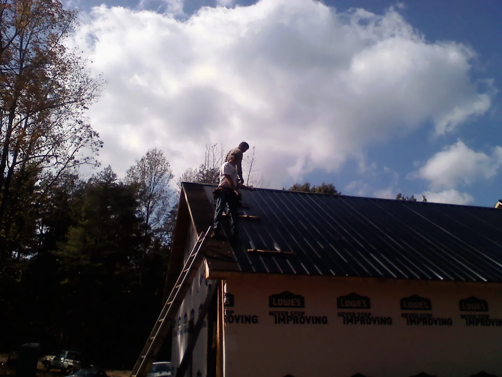 Roofer fastening dark metal panels high against a cloudy sky, from a Roof Inspection job in Indian Valley