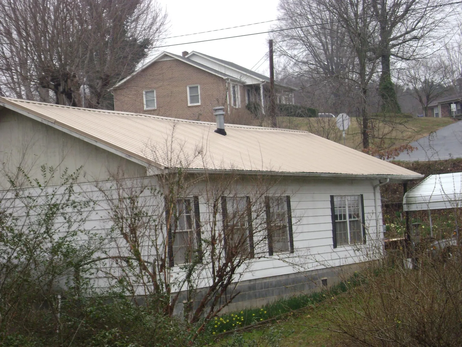 Tan metal roof on a white sided house set into a hillside — Commercial Roofing by Roofing Brothers in Indian Valley